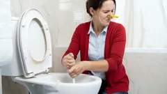 Vrouw ontstopt wc, houdt neus dicht vanwege vieze geur, huishoudelijke klusjes.