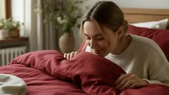 Vrouw ruikt aan fris rood dekbedovertrek op bed in sfeervol ingerichte slaapkamer.