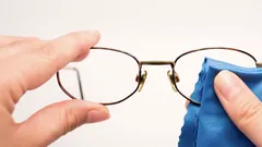 Bril schoonmaken met een blauw microvezeldoekje op een witte achtergrond