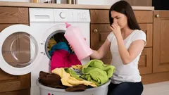 Vrouw ruikt vieze was bij wasmachine en houdt wasmiddel vast