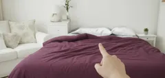 Hand wijst naar bed met paarse deken in lichte slaapkamer interieur