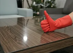 Schone houten tafel met duim omhoog in rode schoonmaakhandschoen