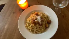 Bord spaghetti carbonara met knapperige stukjes spek, kaarslicht en wijnglas op houten tafel.