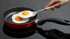Spiegelei bakken in een koekenpan op inductiekookplaat, close-up hand met spatel.