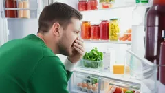 Man ruikt aan koelkast met bedorven eten, vers en ingemaakt voedsel in potten zichtbaar.