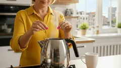 Vrouw zet thee in keuken met fluitketel, stoom stijgt op, zonnige ochtend, huiselijk sfeer
