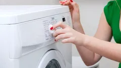 Vrouw stelt het wasprogramma in op een moderne wasmachine in huis.