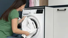 Vrouw laadt wasgoed in een moderne wasmachine in een huiselijke wasruimte.