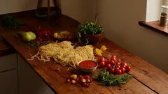 Verse pasta, tomaten, kruiden en pastasaus op houten aanrecht in keuken