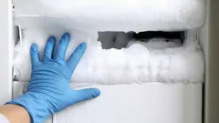 Hand met blauwe handschoen verwijdert ijs uit vriezer, vorstprobleem vriezer schoonmaken