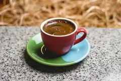 Espressokopje op groen-blauw schoteltje op grijze tafel, vers gezette koffie.