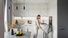 Vrouw in moderne witte keuken gooit afval weg, tafel met fruit, minimalistisch interieur.