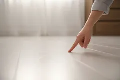 Vinger veegt stof op witte vloer bij raam, schoonmaak huis stof verwijderen.