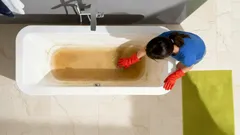 Vrouw met rode handschoenen maakt vuile badkuip schoon vanuit bovenaanzicht.
