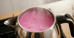 Stalen pan met paarse melk die kookt op een fornuis, stoom komt omhoog.