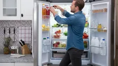 Man pakt drinken uit open koelkast in moderne keuken